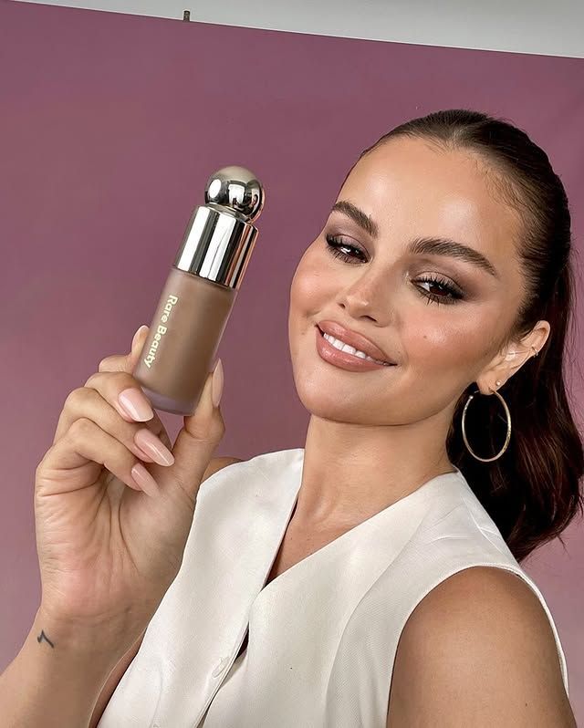 Selena Gomez con un maquillaje brillante y glamoroso sosteniendo el bronceador líquido de belleza rara