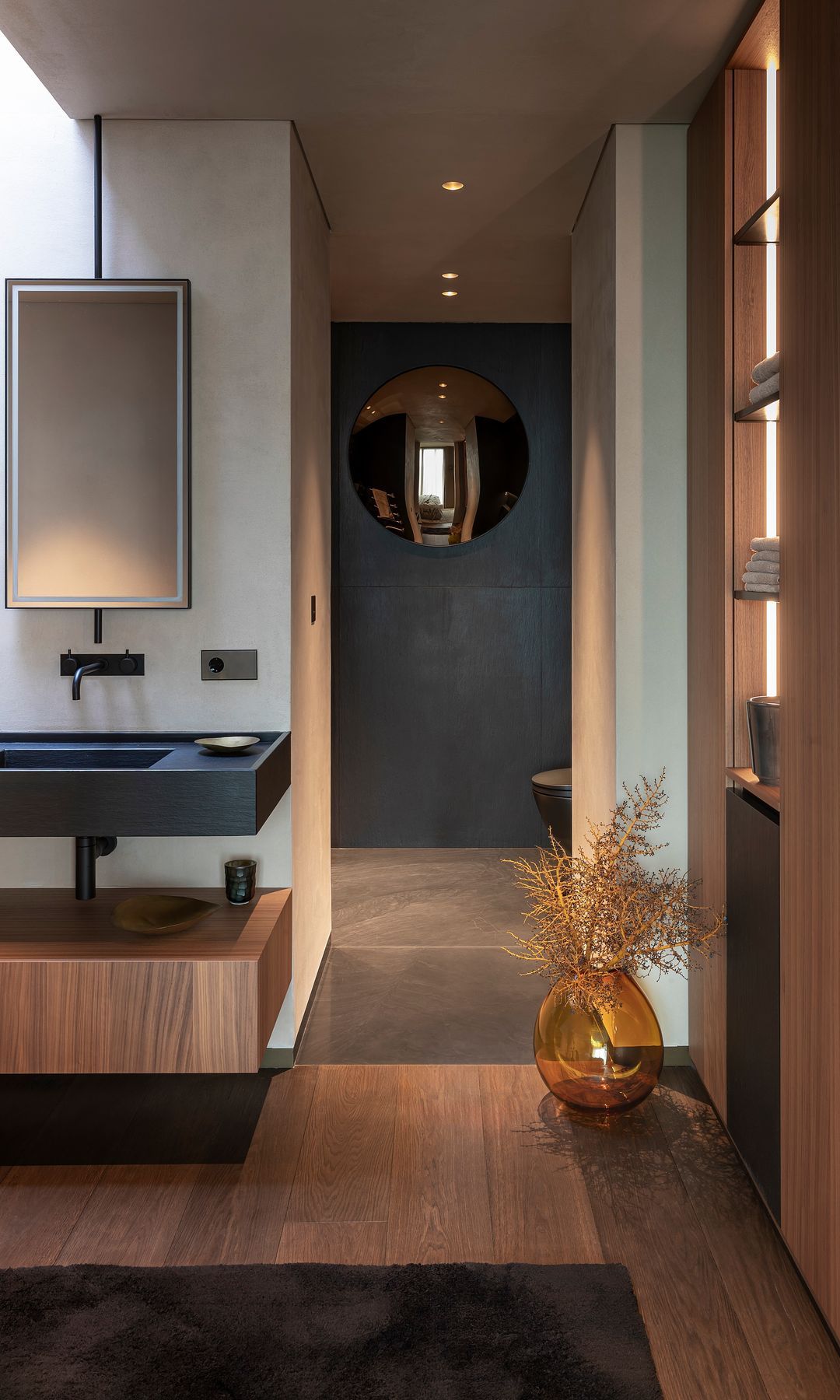 Baño con paredes de madera, negro, estantes y efecto redondo de espejo