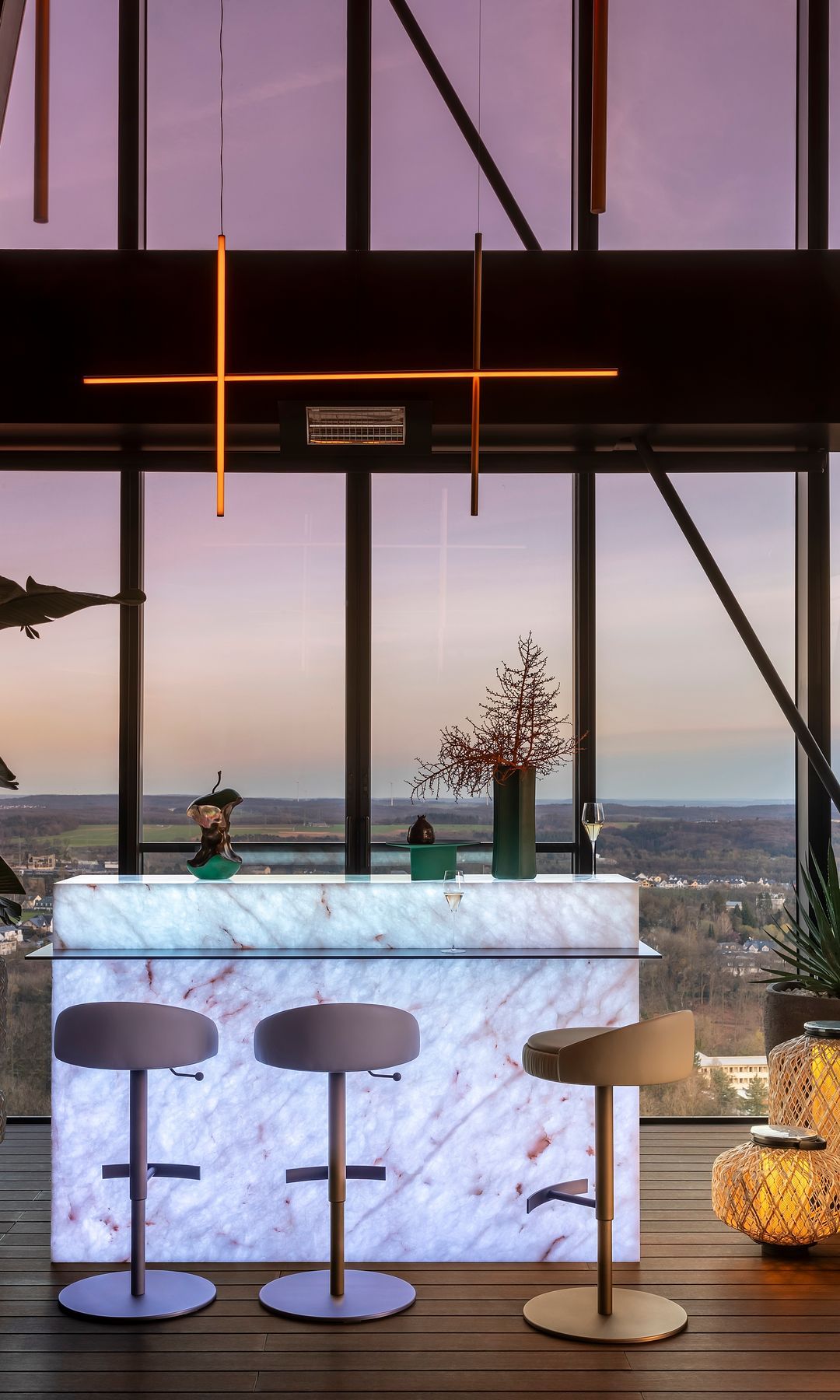 Sala de estar con ventanas grandes, barra retroiluminada, taburetes y lámpara de techo
