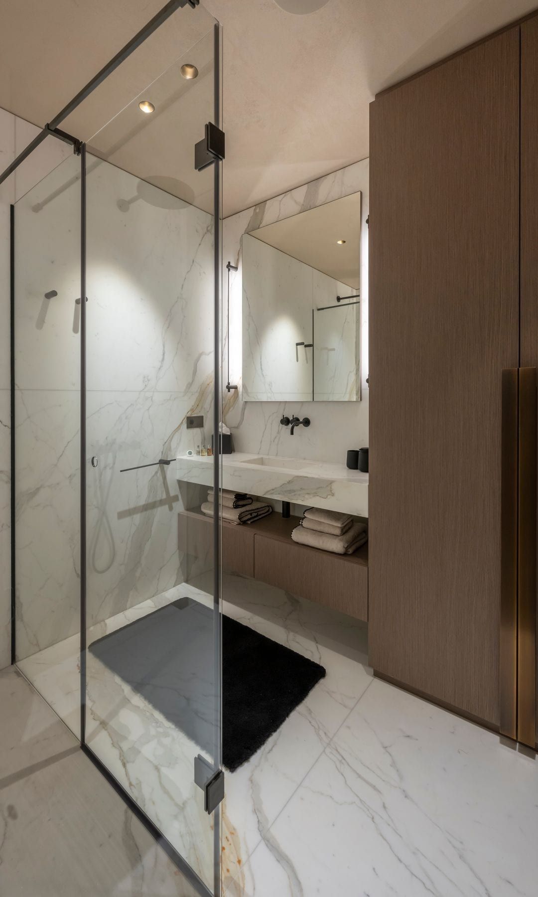 Baño con paredes de tierra y mármol, pantalla de ducha, armario de madera, espejo